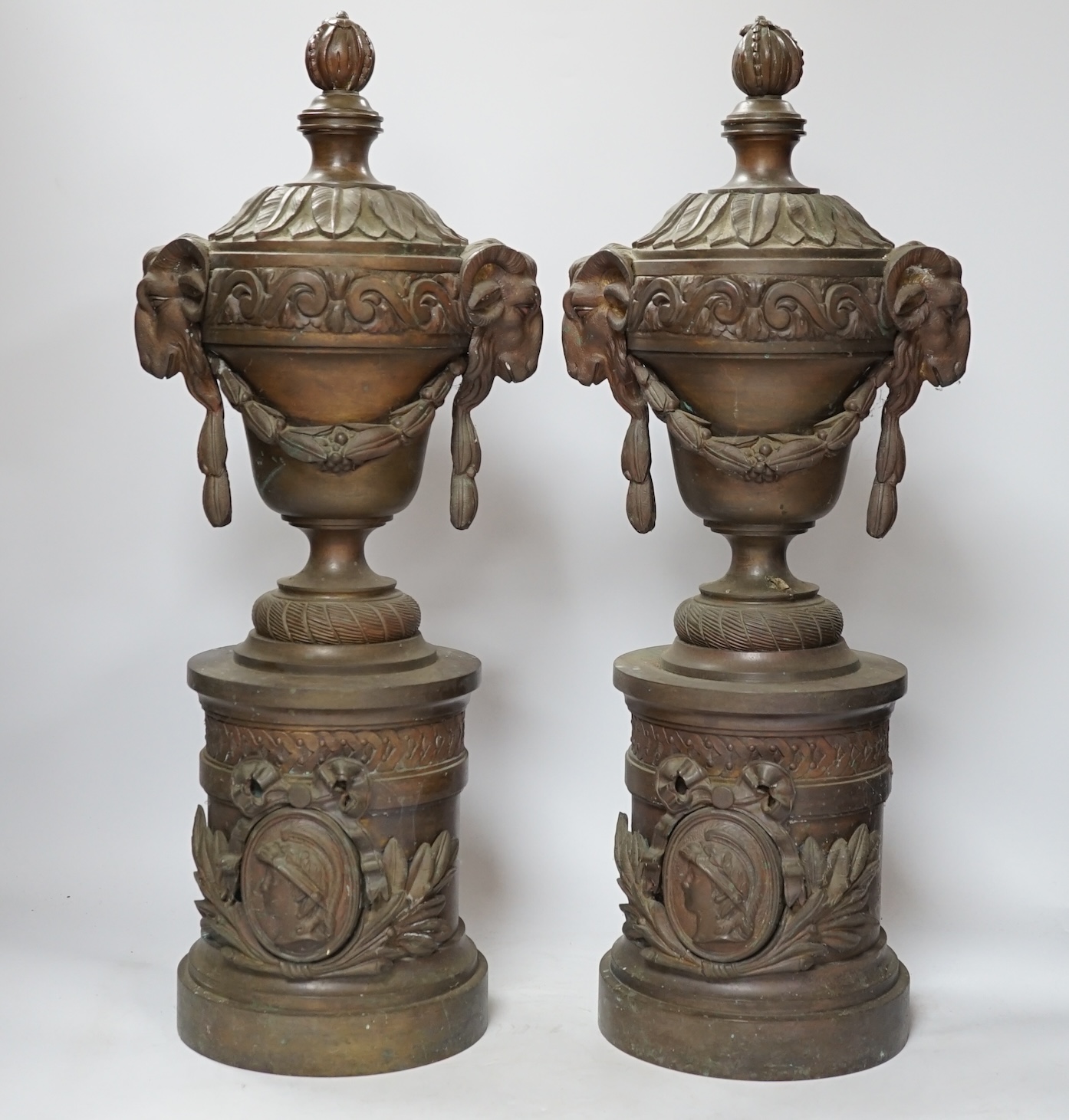 A pair of bronze urns with rams head, Roman mask and swag decoration, 53cm high